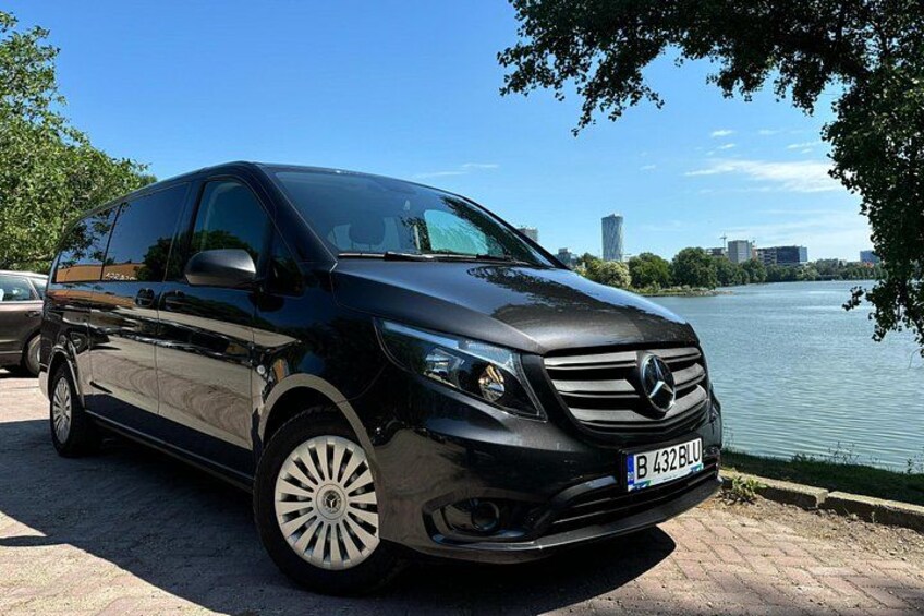 A black Mercedes-Benz SUV parked by a waterfront with a city skyline in the background. 4