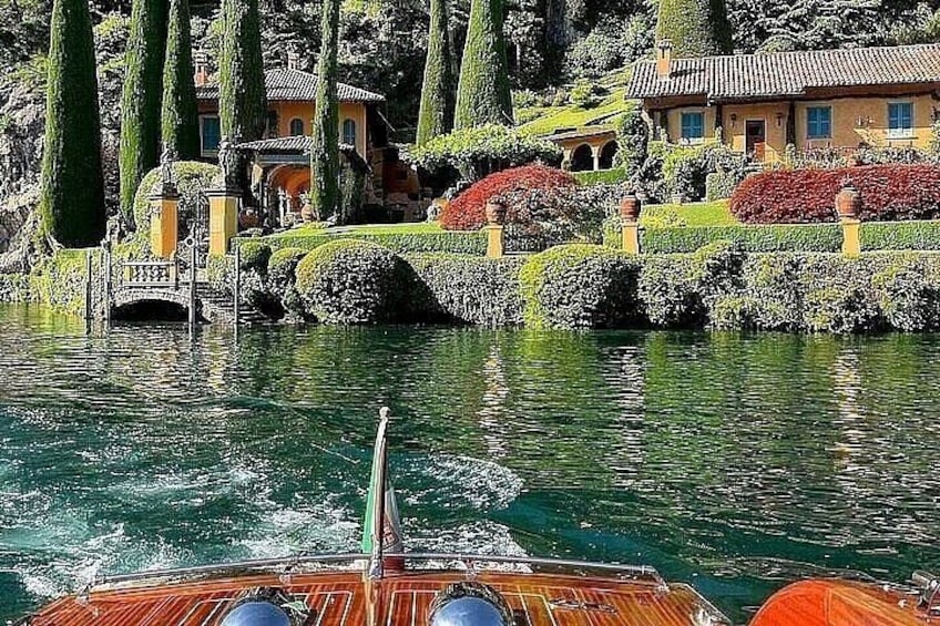 A boat on a lake with a bridge, manicured gardens, and a house in the background. 1