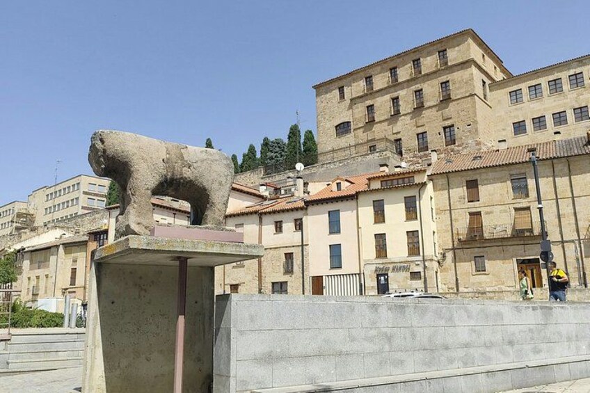 A stone bear statue on a pedestal, buildings in the background, and a clear sky. 2