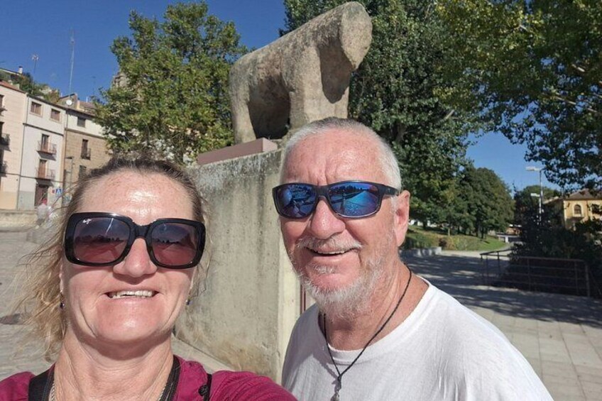 Two people standing in front of a stone structure with trees and buildings in the background. 5