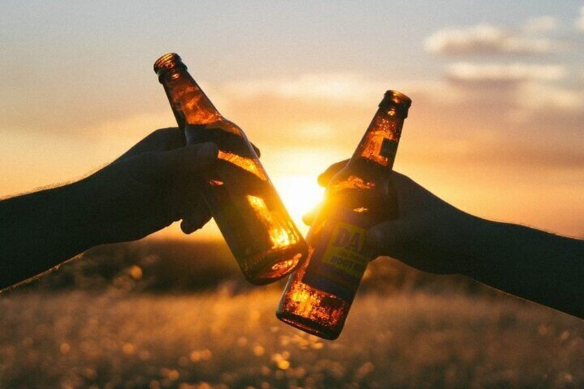 Two hands holding beer bottles with the sun setting in the background. 4