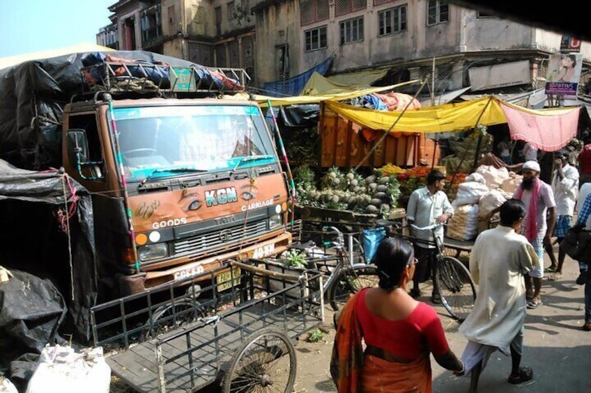 Ein belebter Markt mit einem parkenden Lastwagen, Fußgängern und einem Fahrrad. 2