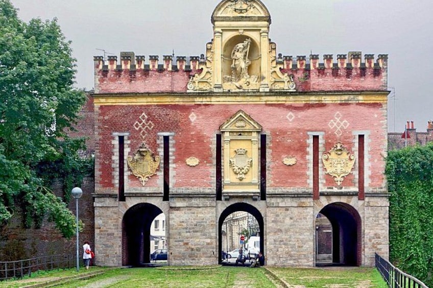 A historic building with a central archway, decorative coats of arms, and a statue on top. 2