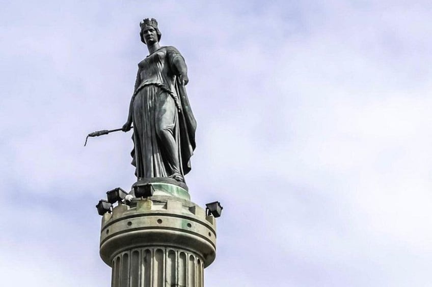 A statue of a woman holding a torch, standing on a column with a circular base. 5