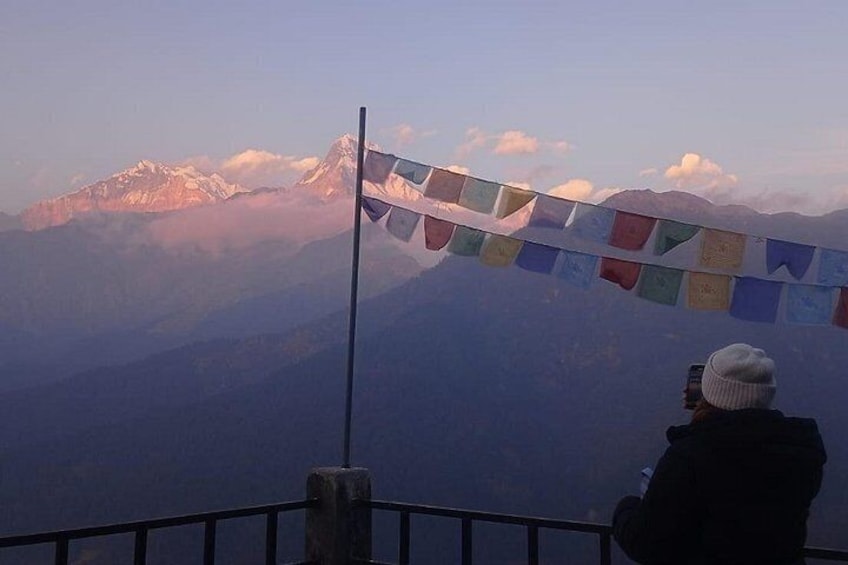A person taking a photo of a mountain range with prayer flags. 1