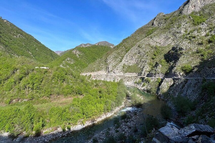A mountainous landscape with a river, a bridge, and lush greenery. 2