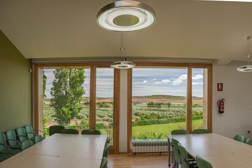 Ein Konferenzraum mit einem großen Tisch, grünen Stühlen und Blick auf eine ländliche Landschaft durch große Fenster. 2