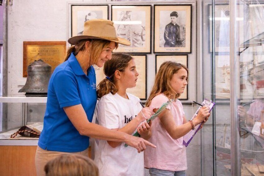 Una persona con camisa y gorra azul, de pie junto a dos niños con camisas blancas, uno sosteniendo un portapapeles. 3