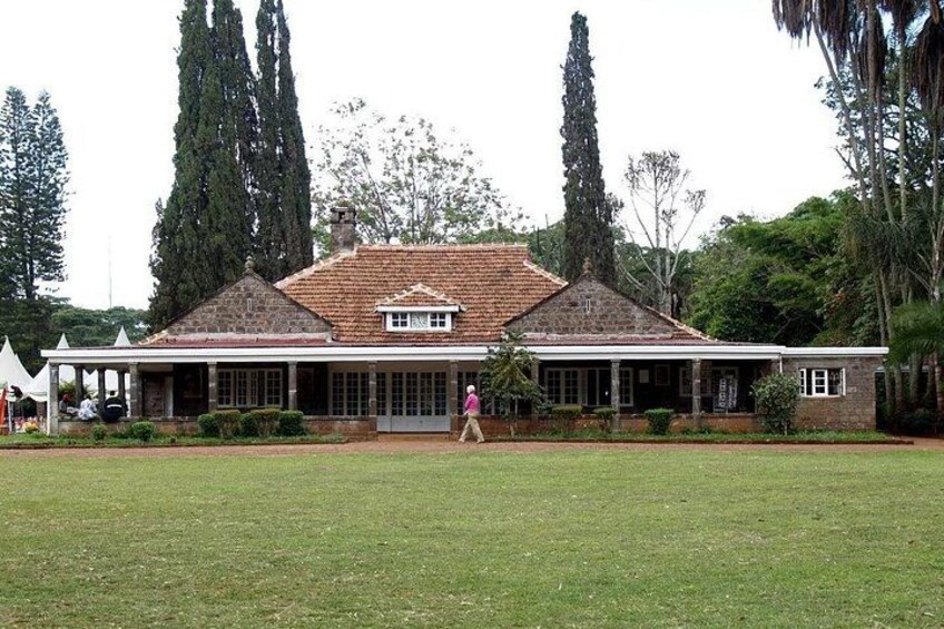 A large brick building with a tiled roof, surrounded by a grassy lawn and tall trees. 2