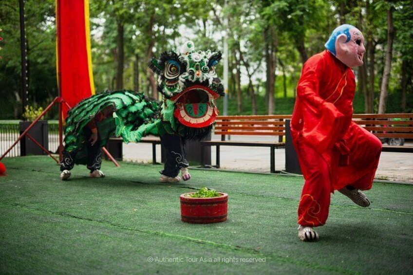 A person in a red costume performing a lion dance with a green lion head. 2