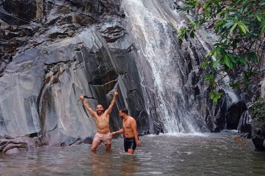Two people standing in a shallow stream with a waterfall in the background. 3