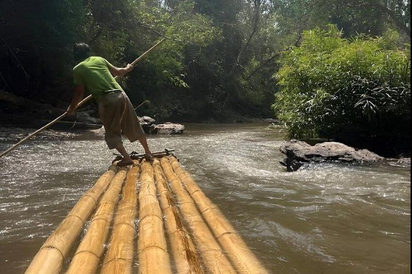 A person standing on a bamboo raft in a river surrounded by dense greenery. 5
