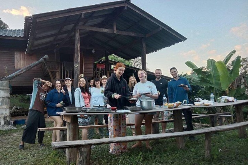 A group of people gathered around a wooden table with cooking equipment, under a rustic shelter. 5