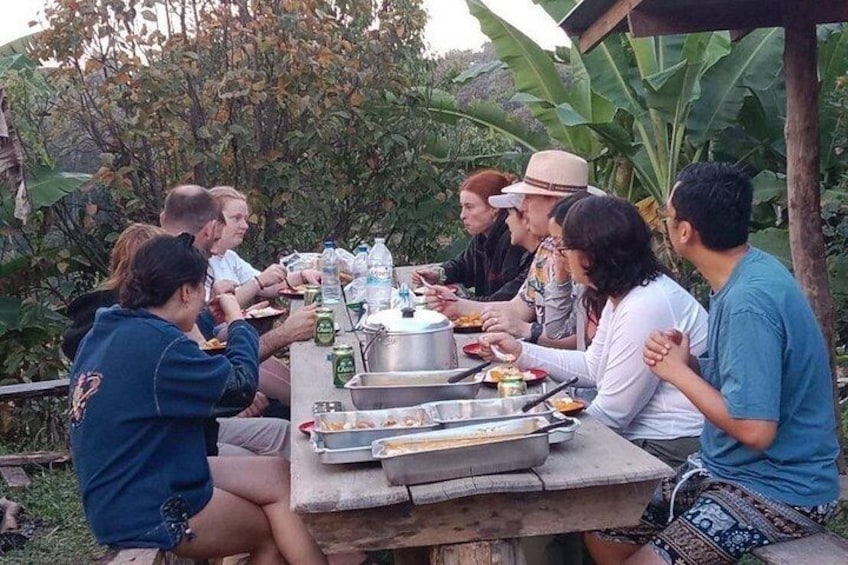 A group of people sitting around a table outdoors, eating and drinking. 4