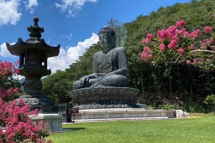 A large Buddha statue in a garden with a pagoda and pink flowers. 4