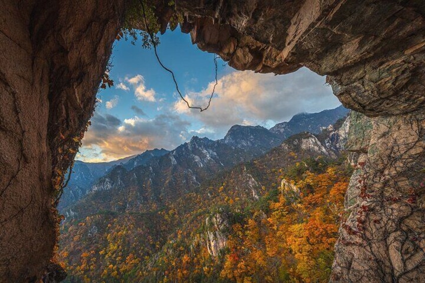 A mountainous landscape with autumn foliage, a rocky overhang, and a clear sky. 3