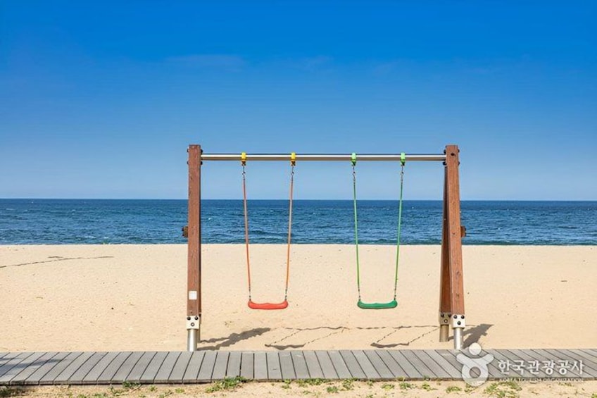 A wooden swing set on a sandy beach with the ocean in the background. 2