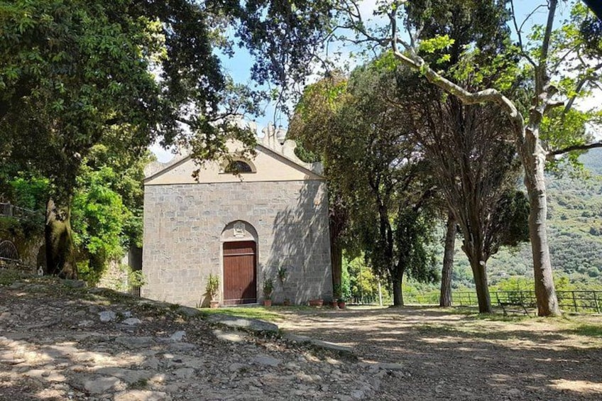 A stone building with a red door, surrounded by trees and a gravel path. 1