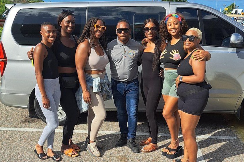 A group of people standing in front of a silver van. 2