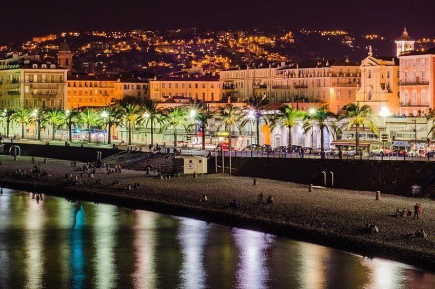 A coastal cityscape at night with illuminated buildings, a beach, and palm trees. 2