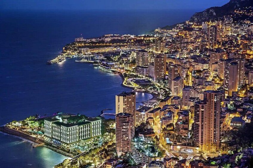 A coastal cityscape at night with illuminated buildings and a marina. 1