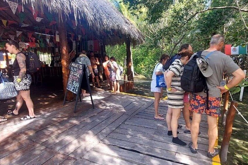 Une terrasse en bois où se trouvent des personnes debout et qui se promènent, une structure dotée d’un toit de chaume et une enseigne avec du texte. 2