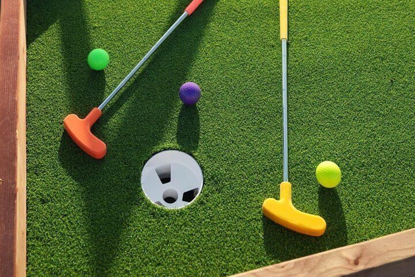 Ein Minigolfplatz mit grünem Kunstrasen, einem weißen Loch und Golfschlägern. 4