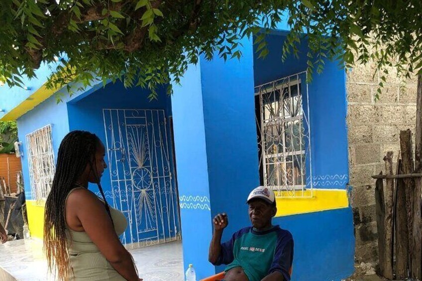Two people standing in front of a blue building with a yellow stripe and a metal gate. 4