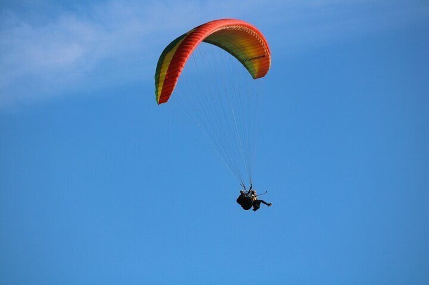 A paraglider with a red and yellow parachute against a clear blue sky. 3