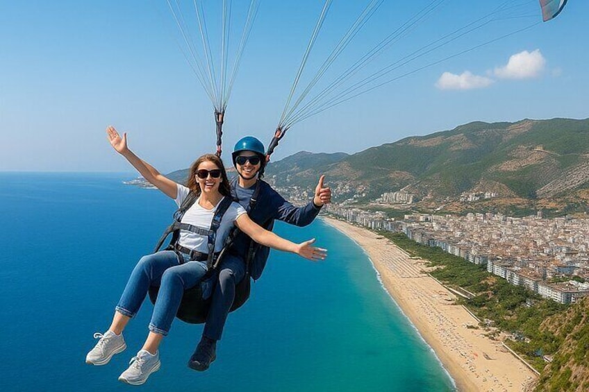 Two people paragliding over a coastal area with a beach and cityscape below. 1