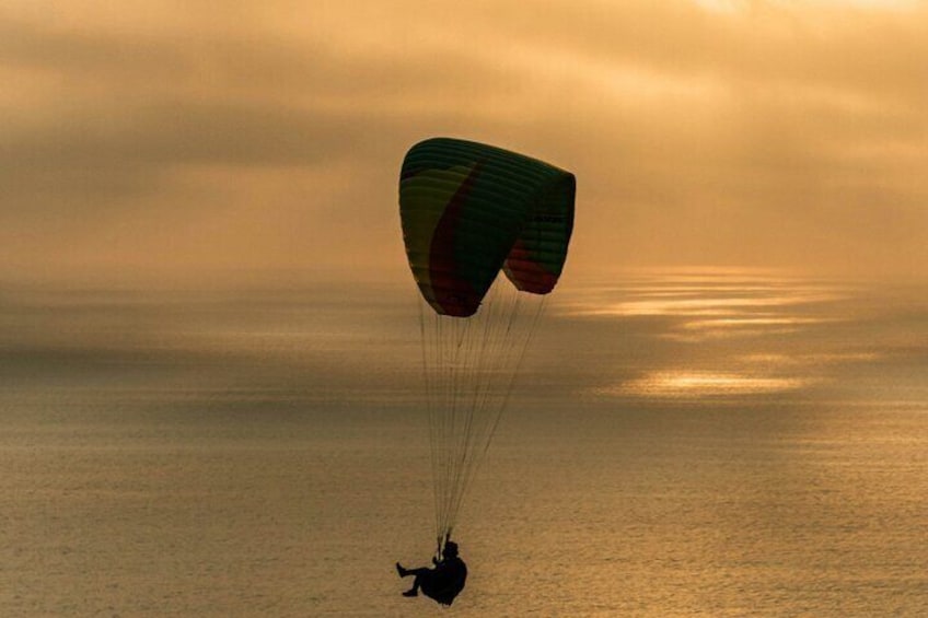 A person paragliding over a body of water during sunset. 4