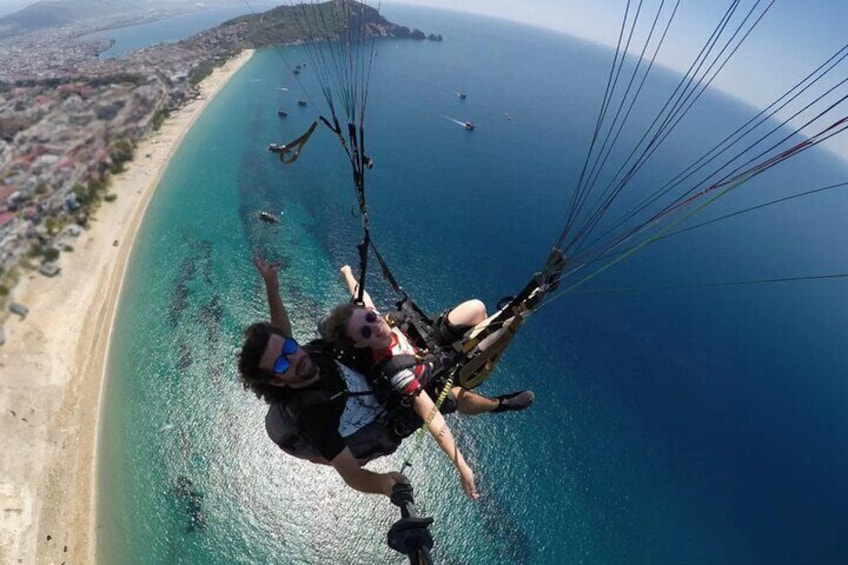 A person paragliding over a coastal area with a beach and clear blue sea. 5
