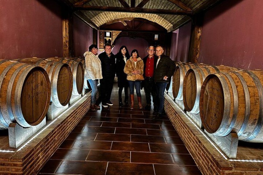 A group of people standing in a wine cellar with wooden barrels. 1
