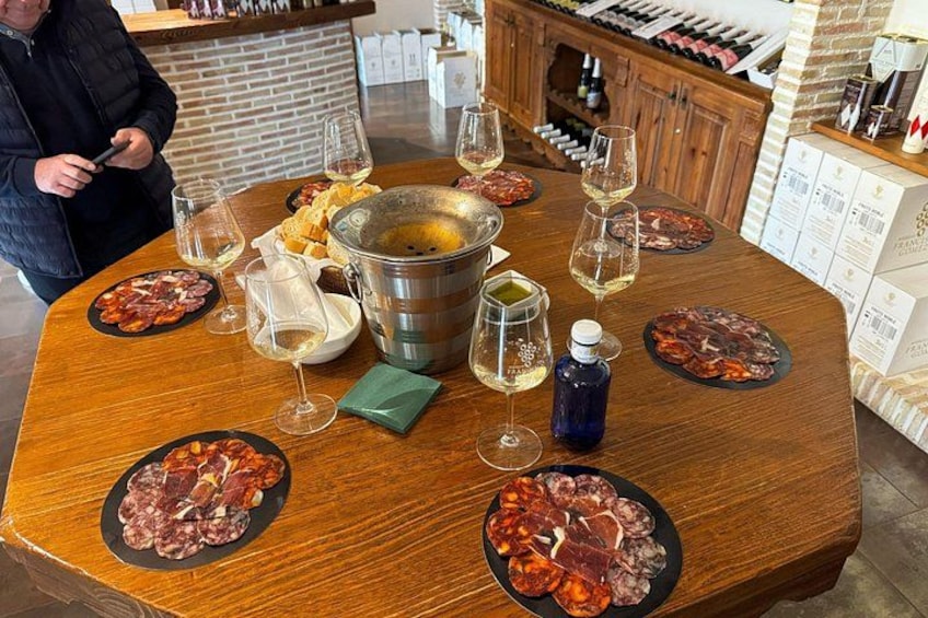 A round wooden table with plates of cured meats, glasses of wine, and a metal pot. 3