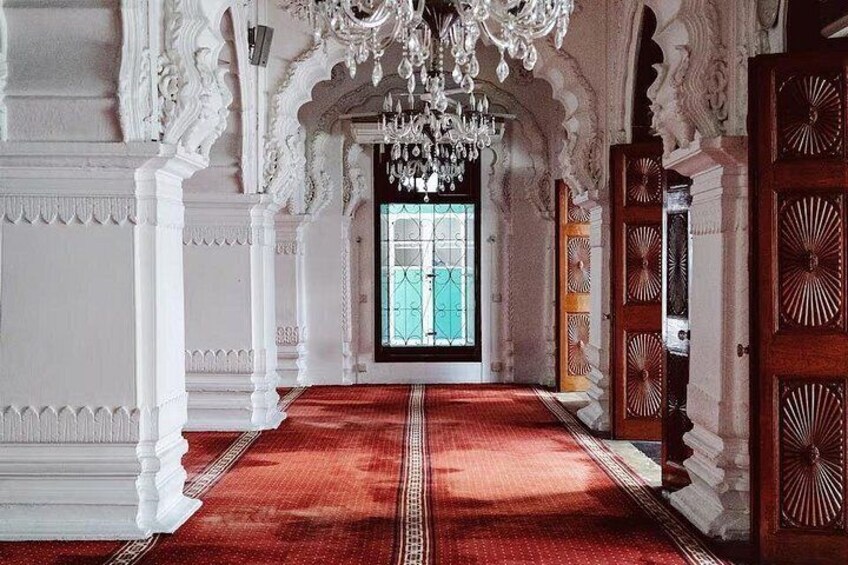 An ornate hallway with a red carpet, white columns, and a chandelier. 2