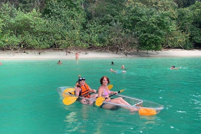 Dos personas kayakendo en aguas turquesas con una playa y follaje denso al fondo. 1