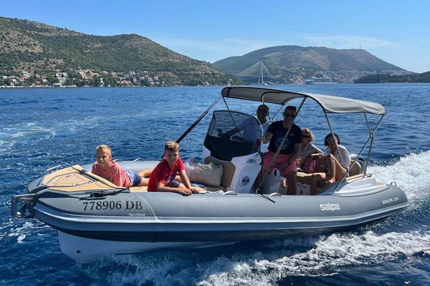 En motorbåd med mennesker ombord sejler på vandet med et bakket landskab i baggrunden. 5