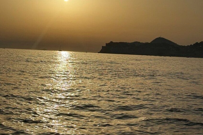 A sunset over a body of water with a silhouette of a hill or mountain in the background. 2