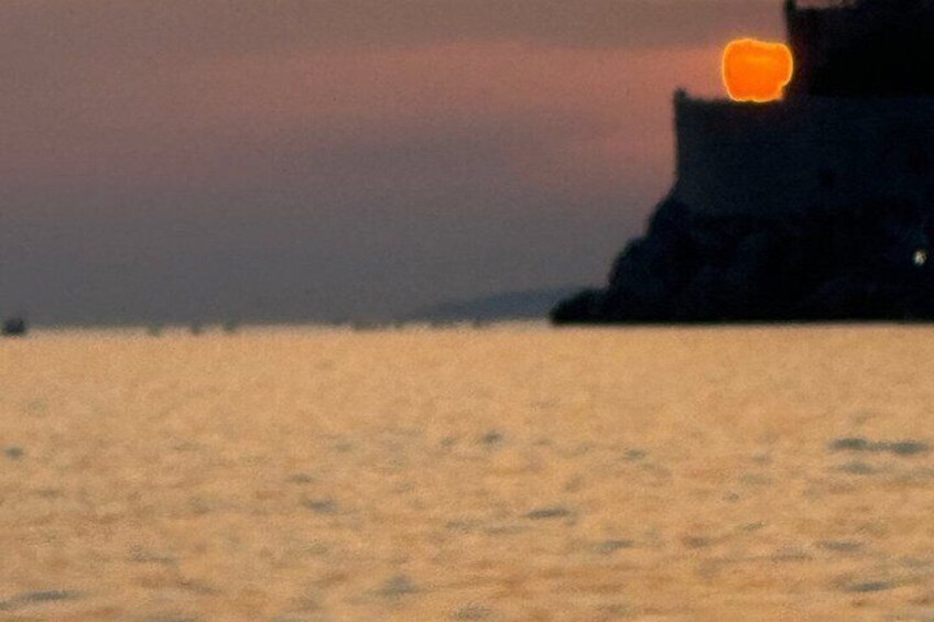 A sunset over a body of water with a rocky outcrop in the distance. 1