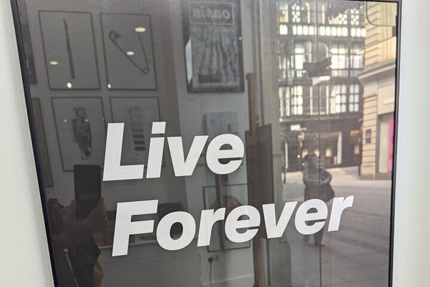 Fachada con el letrero "Live Forever" y obras de arte enmarcadas en la pared. 1