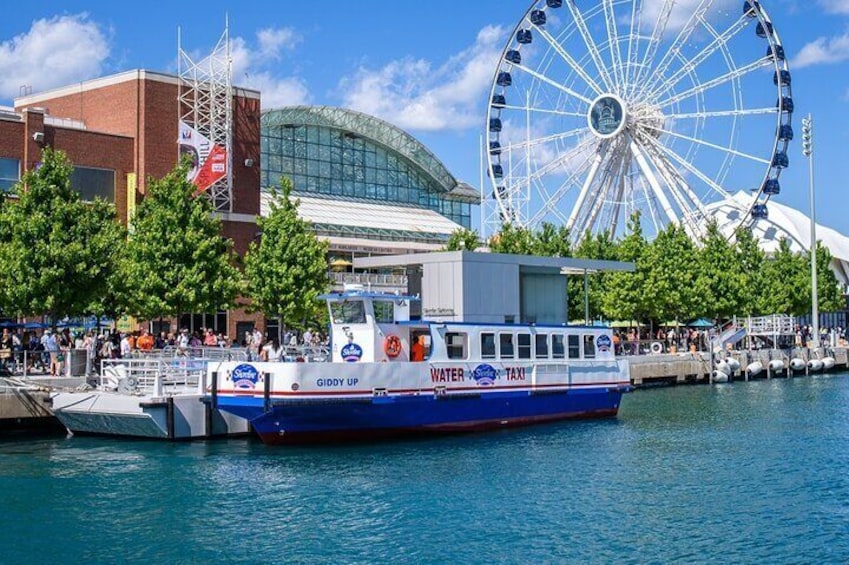 A water taxi named Giddy Up on a river with a Ferris wheel and a stadium in the background. 5