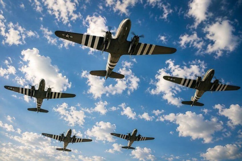 Four vintage military aircraft flying in formation against a blue sky with scattered clouds. 1