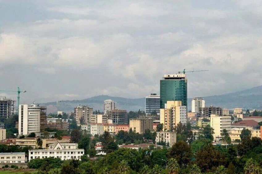 Un paisaje urbano con varios edificios, incluyendo un rascacielos verde destacado, bajo un cielo nublado. 4