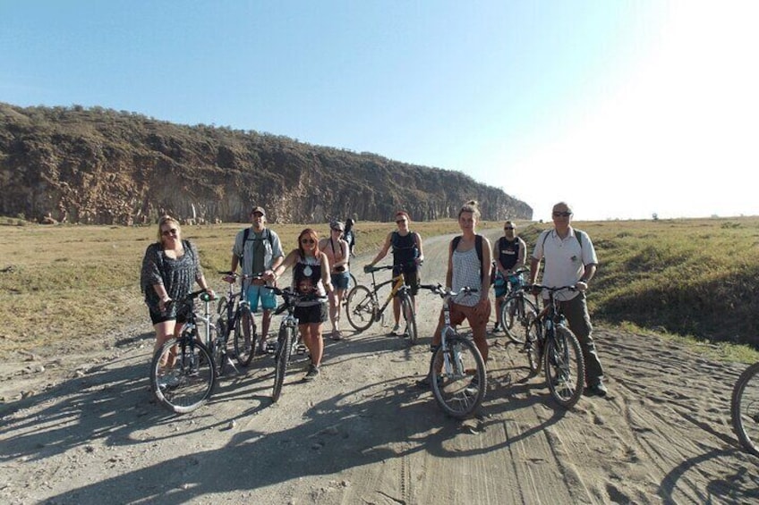 Un grupo de personas en bicicleta por un sendero arenoso, con una colina boscosa al fondo. 1