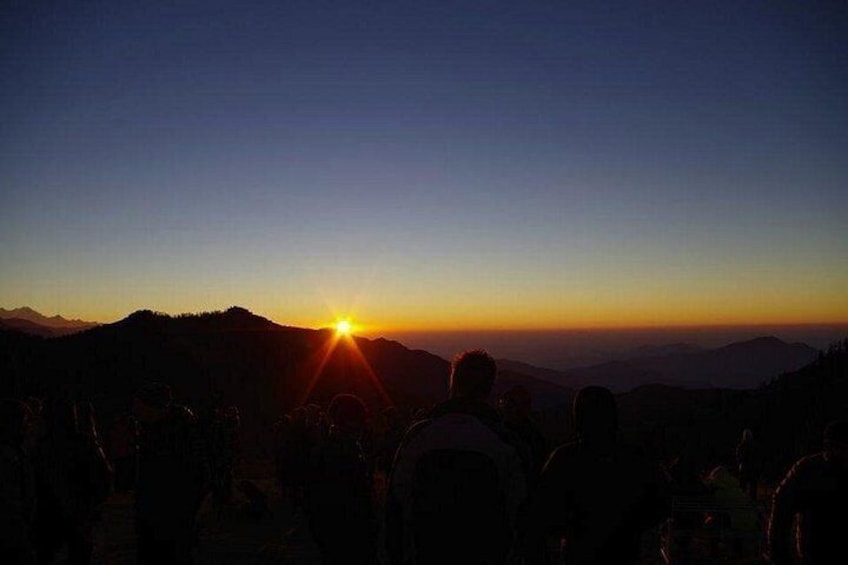 A sunset over a mountainous landscape with silhouettes of people. 4