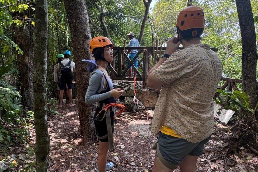Un área boscosa con gente usando cascos y arneses, sugiriendo una actividad guiada como tirolesa o rappel. 4