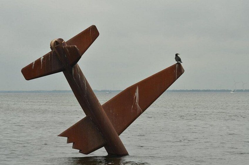 A rusted metal structure in the water with a bird perched on it. 2