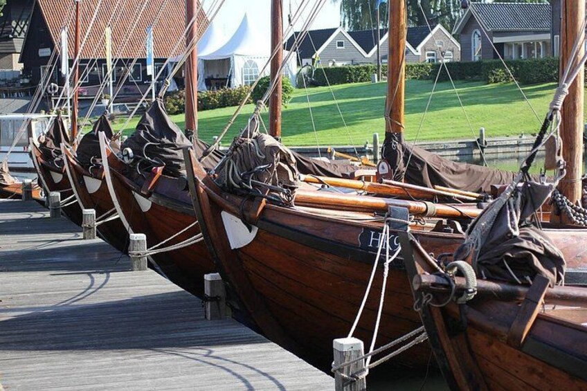 A row of wooden boats docked at a pier with a building and greenery in the background. 3
