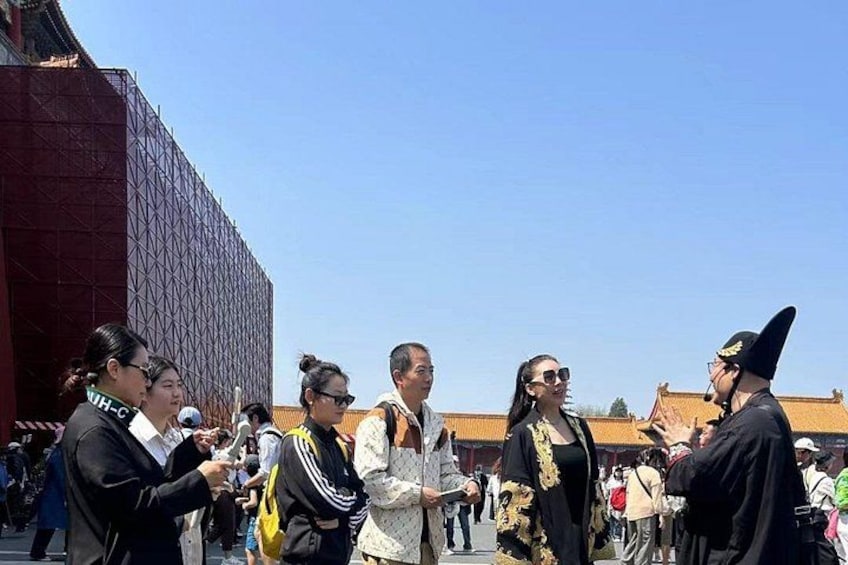 Un gruppo di persone in piedi all'aperto, alcune in abiti tradizionali, con un grande edificio sullo sfondo. 4