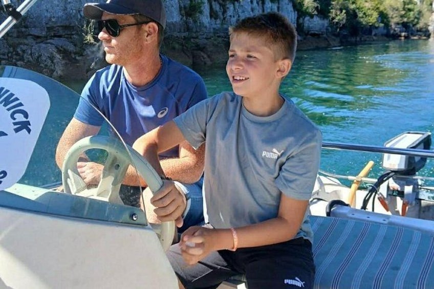 Two people on a boat with a rocky shoreline in the background. 4